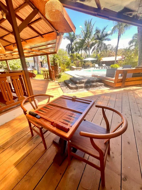 A wooden backgammon table and two chairs on the deck, with the pool in the background.