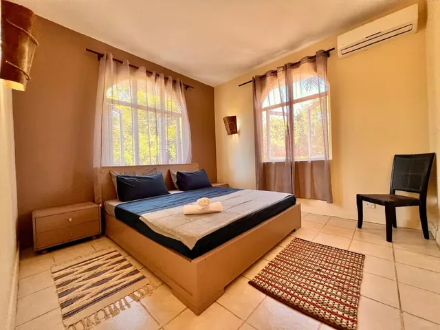 A lodge bedroom with a large bed, air conditioning and two arched windows.