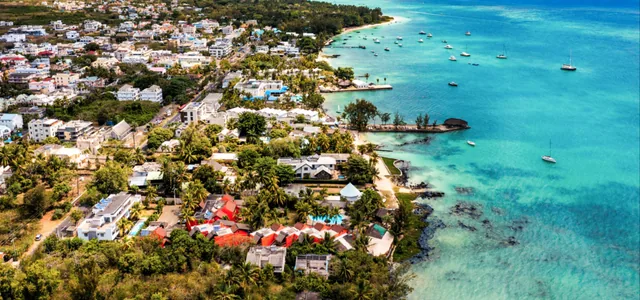 Grand Baie from the air, with the town along the shore and boats moored in a turquoise bay.