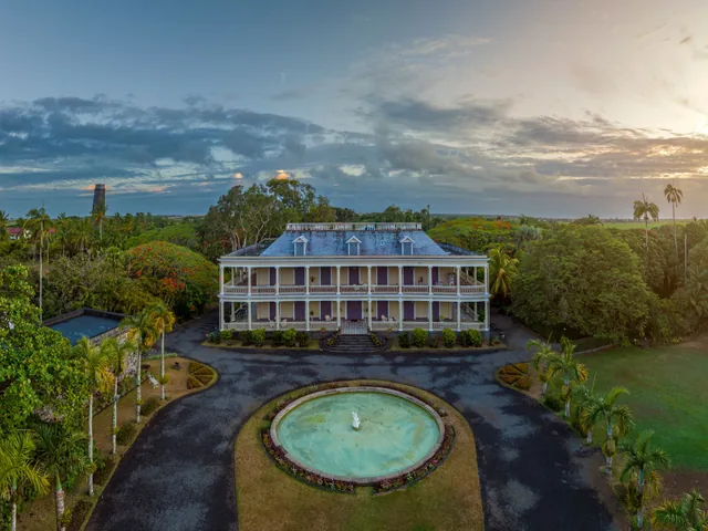 A white colonial house with a round fountain and gardens, seen from above.