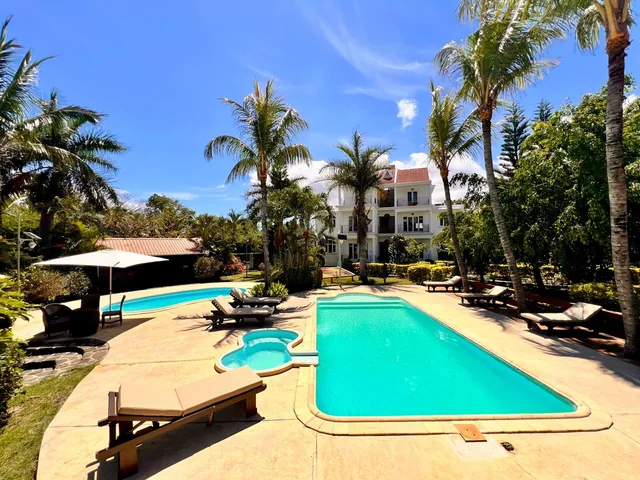 A pool with sun loungers and a smaller round pool beside it, under palm trees.